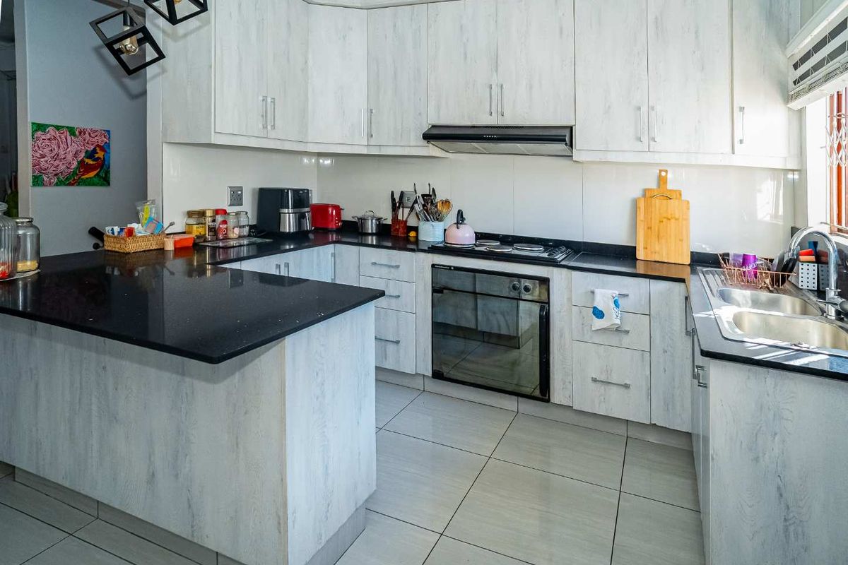 Modern kitchen featuring light wood-grain cabinetry, black granite countertops, built-in oven, hob, extractor fan, and double stainless steel sink.
