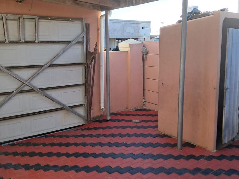 A covered outdoor patio area featuring patterned paving, a garage entrance, and a boundary wall, providing a functional utility space.