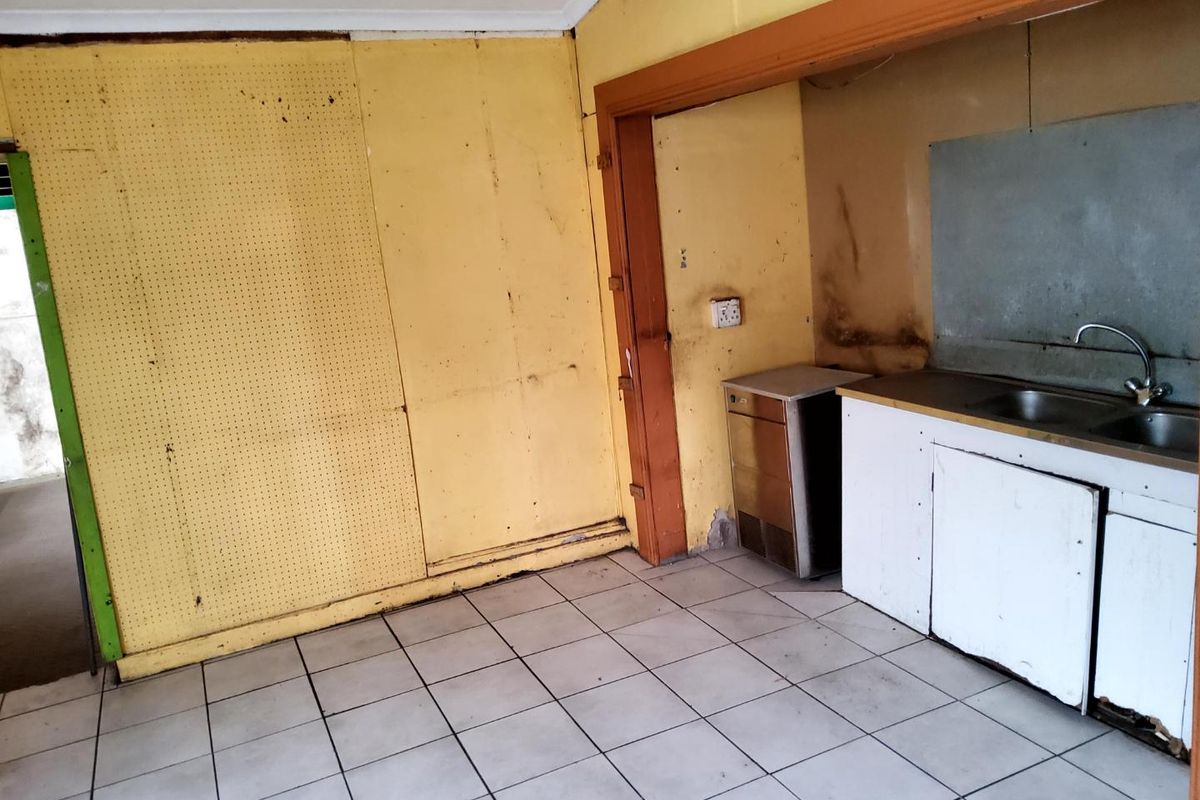 A small, dated kitchenette area featuring tiled flooring, a basic sink unit, and worn wall paneling, requiring significant refurbishment.