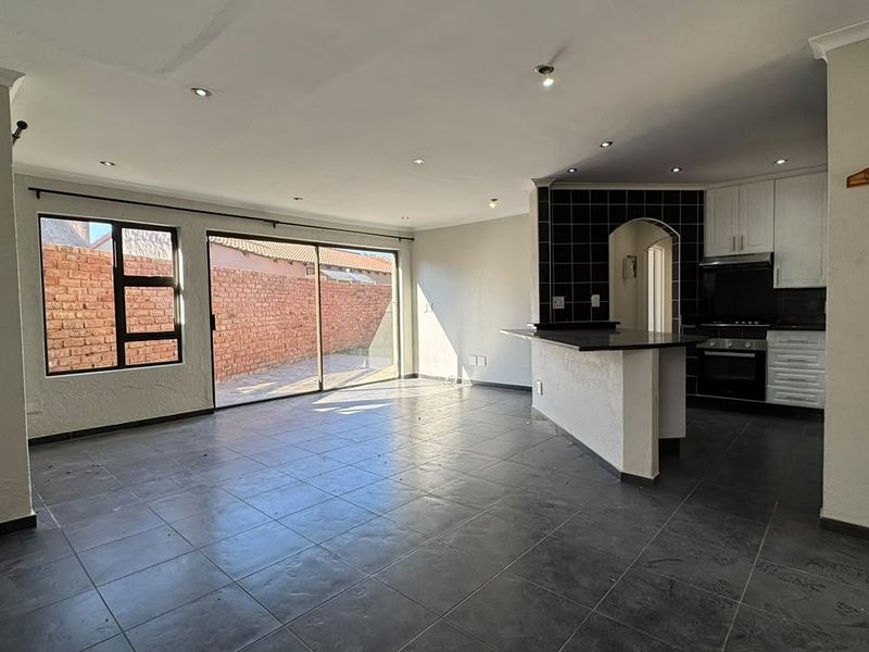 Spacious open-plan living area featuring tiled floors, a kitchen island with built-in appliances, and large sliding doors leading to the rear exterior.