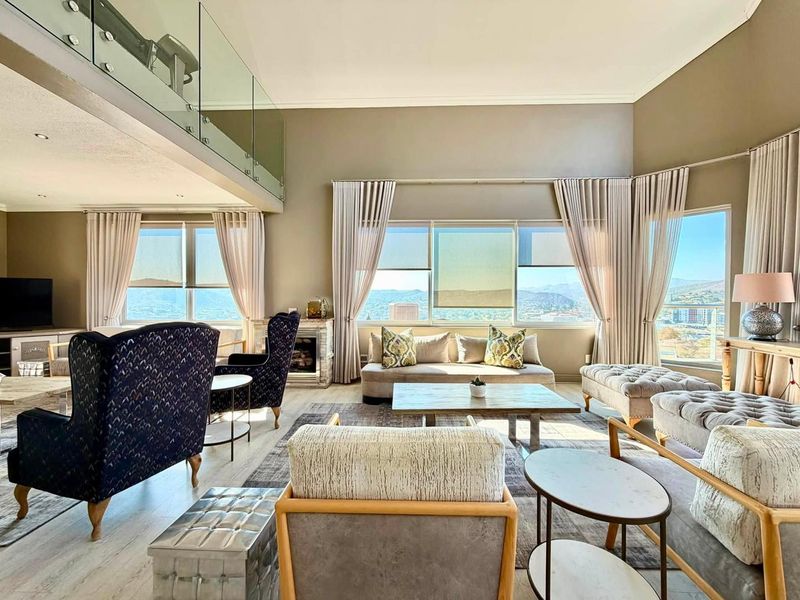 Spacious double-volume living room featuring a glass-railed mezzanine, built-in fireplace, and expansive windows offering panoramic views.
