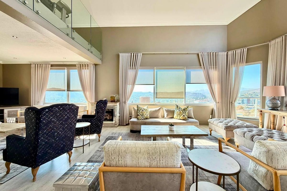 Spacious double-volume living room featuring a glass-railed mezzanine, built-in fireplace, and expansive windows offering panoramic views.