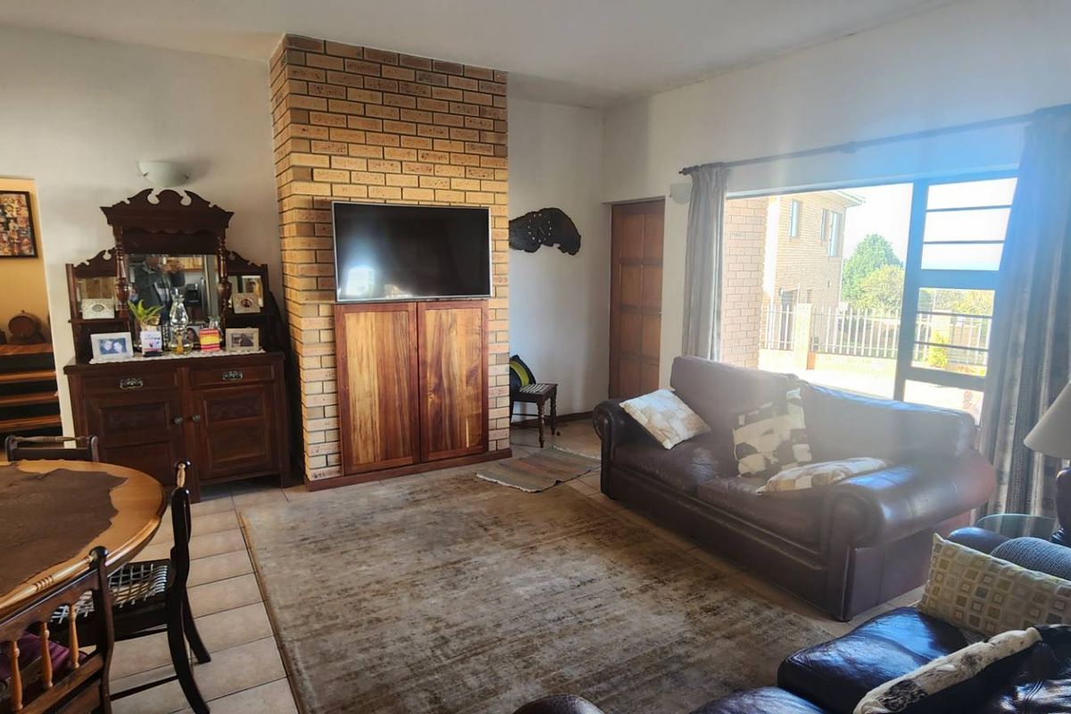 Spacious living area featuring a prominent face-brick fireplace, tiled flooring, and large windows providing natural light and access to the exterior.