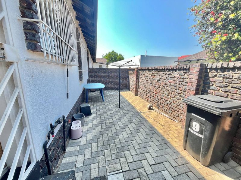 A paved rear courtyard area enclosed by brick boundary walls, featuring external plumbing access and security bars on the windows.