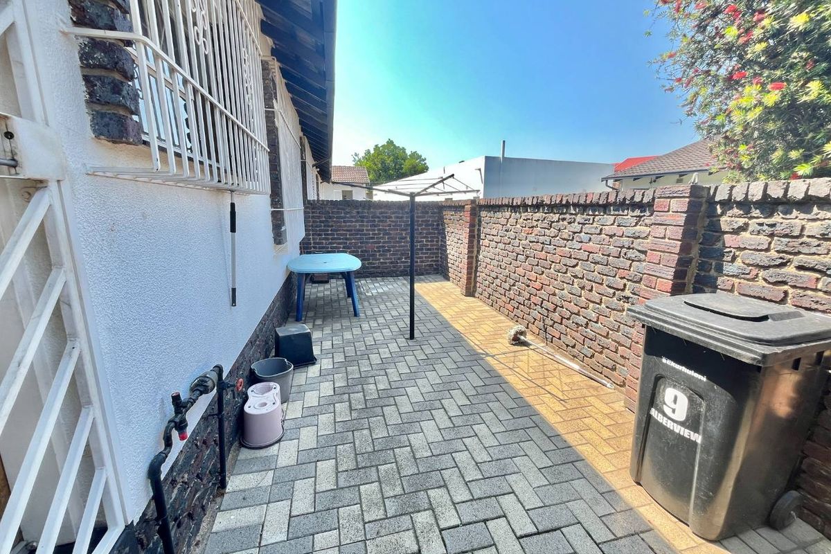 A paved rear courtyard area enclosed by brick boundary walls, featuring external plumbing access and security bars on the windows.