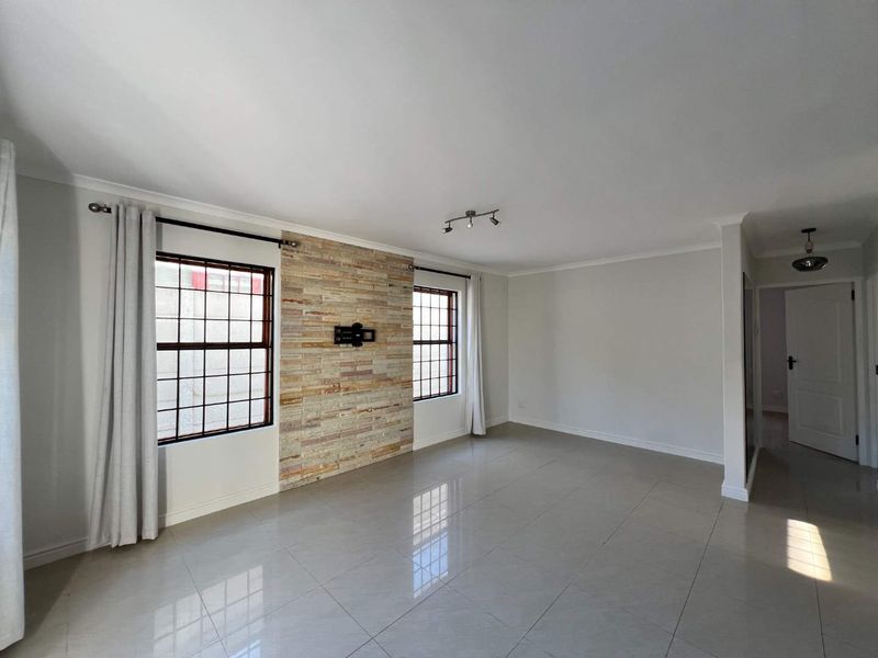 Spacious living room featuring polished tile flooring, a decorative stone feature wall, and large windows with security bars.