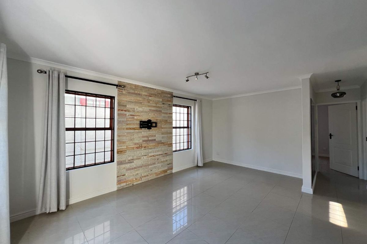 Spacious living room featuring polished tile flooring, a decorative stone feature wall, and large windows with security bars.