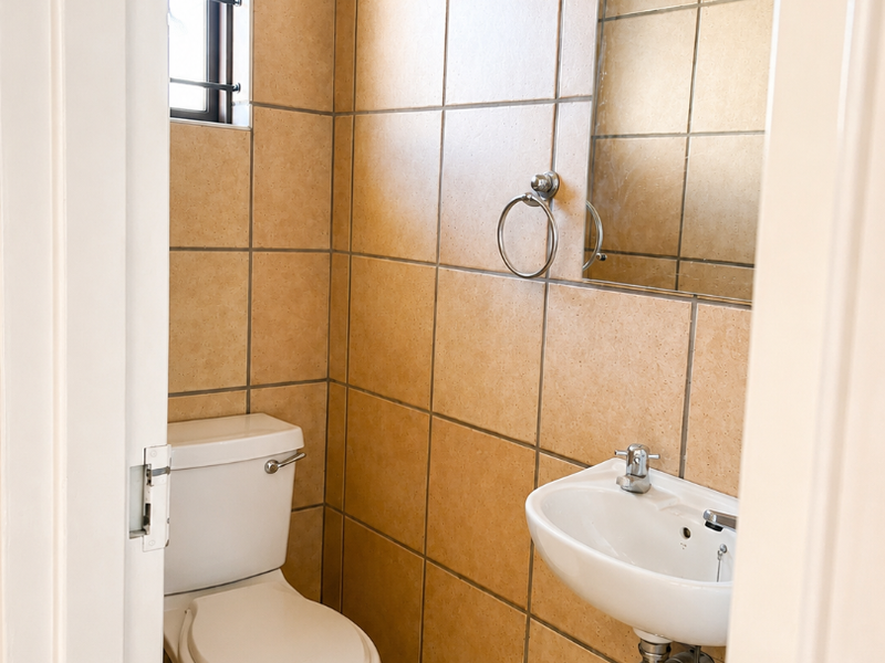 A compact guest bathroom featuring floor-to-ceiling ceramic tiling, a wall-mounted basin, and a standard toilet.