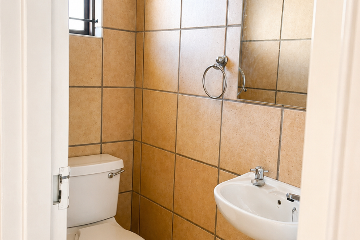 A compact guest bathroom featuring floor-to-ceiling ceramic tiling, a wall-mounted basin, and a standard toilet.