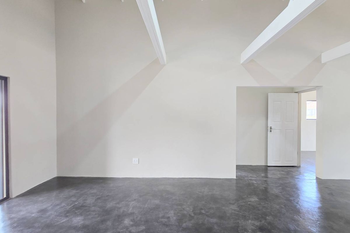 Spacious living area featuring high vaulted ceilings with exposed beams, polished concrete flooring, and direct access to an outdoor patio.