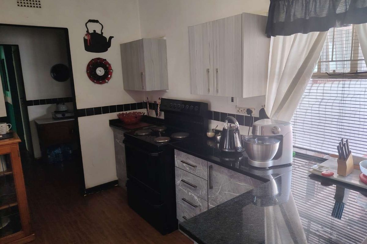 A functional kitchen featuring granite countertops, built-in cabinetry, and a freestanding electric stove, with a view into the adjacent hallway.