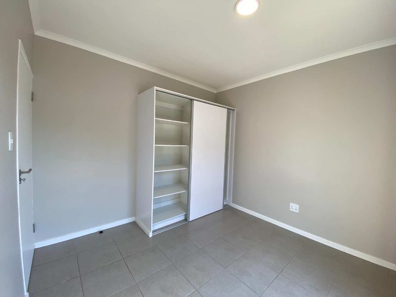 A clean, empty bedroom featuring neutral wall paint, tiled flooring, and a functional built-in wardrobe with sliding doors.