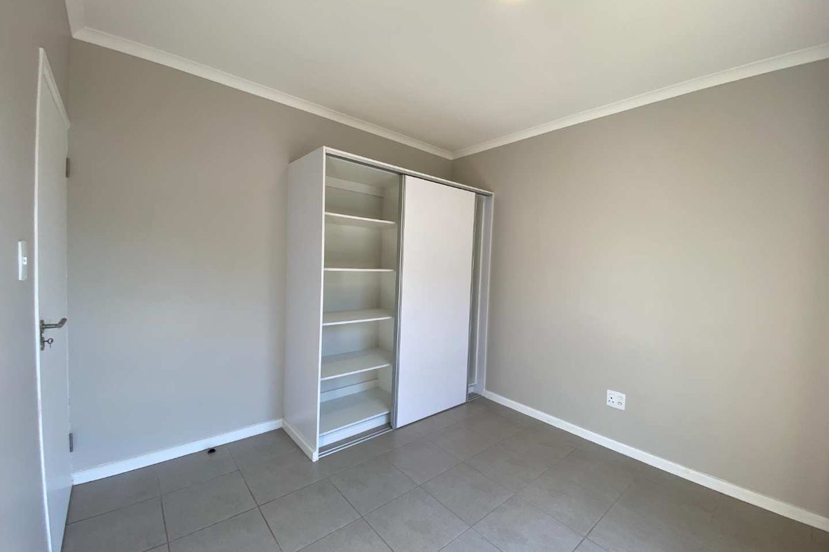 A clean, empty bedroom featuring neutral wall paint, tiled flooring, and a functional built-in wardrobe with sliding doors.