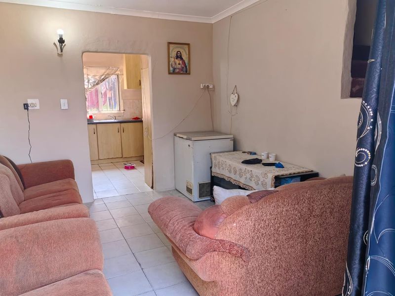 A living room area with tiled flooring and coved ceilings, featuring an open transition to the adjacent kitchen space.