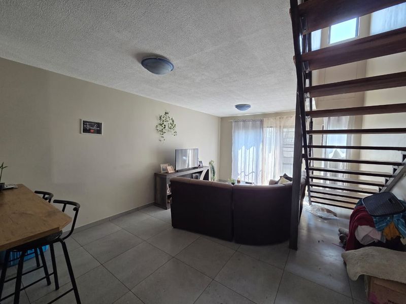 Open-plan living area featuring tiled flooring and a wooden staircase leading to the upper level, with access to a patio through sliding glass doors.