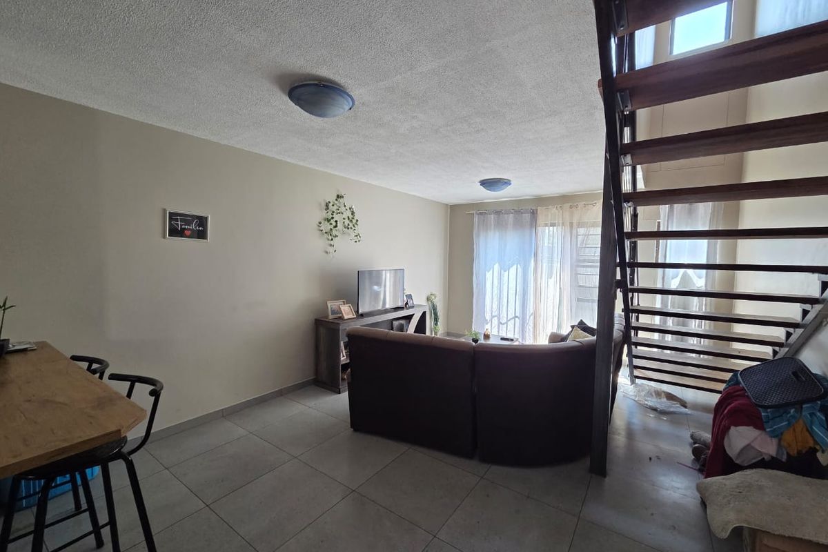 Open-plan living area featuring tiled flooring and a wooden staircase leading to the upper level, with access to a patio through sliding glass doors.