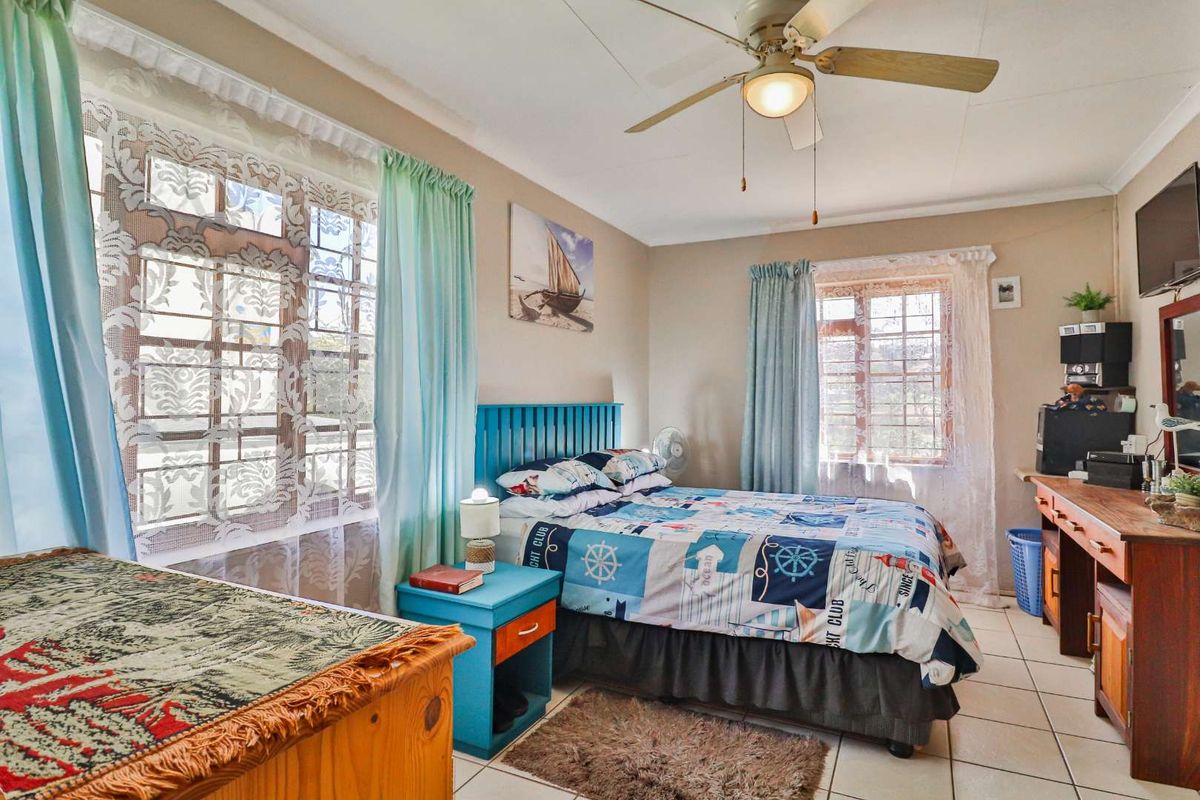 A bedroom featuring tiled flooring, a ceiling fan, and security bars on the windows.