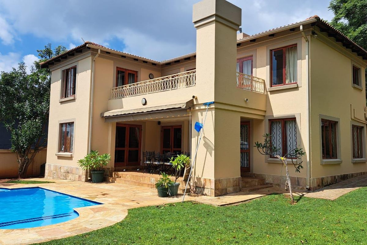 Rear view of a two-story house featuring a swimming pool, stone patio, and an upper-level balcony with metal railings.