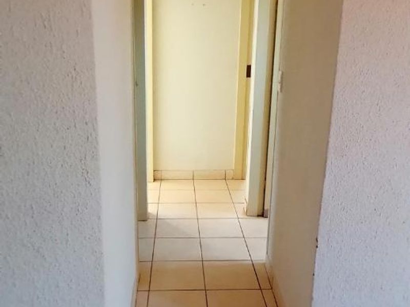 A simple, empty hallway featuring neutral tiled flooring and textured wall finishes, providing access to multiple rooms.