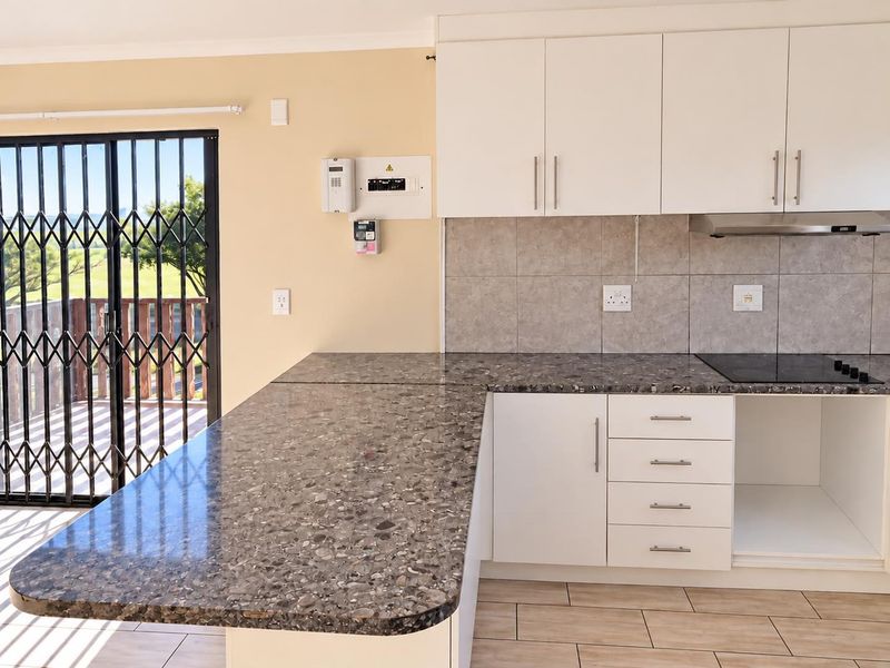 Modern kitchen featuring white cabinetry, stone-look laminate countertops, an electric hob with extractor, and direct access to an outdoor balcony through a security gate.