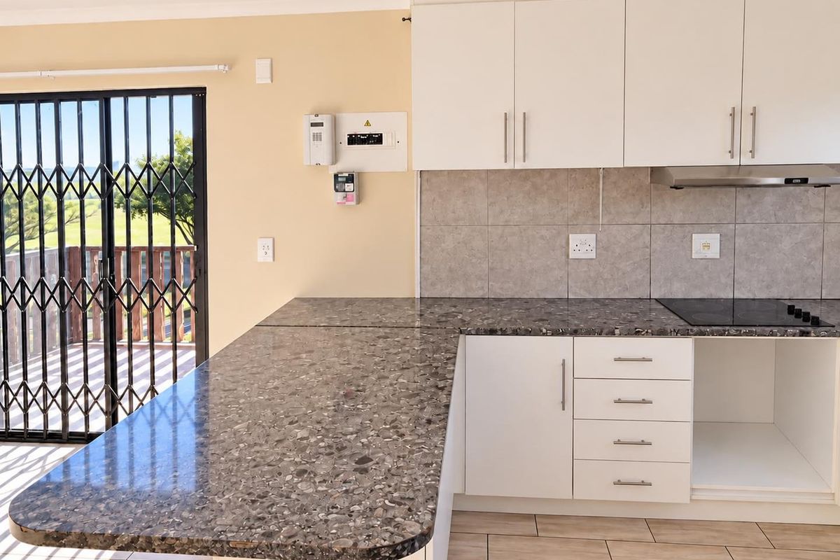 Modern kitchen featuring white cabinetry, stone-look laminate countertops, an electric hob with extractor, and direct access to an outdoor balcony through a security gate.