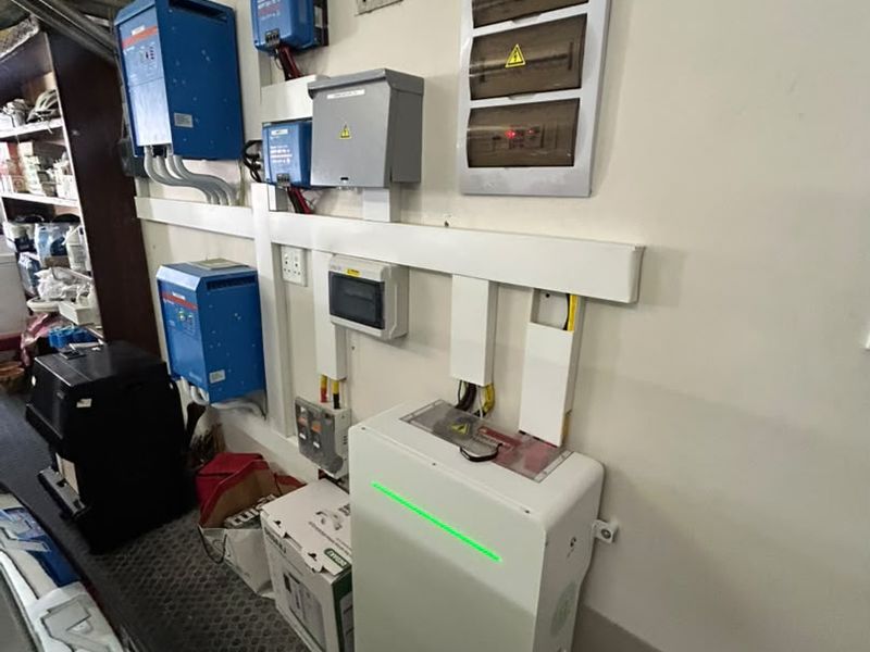 Utility area featuring a modern solar power system with inverter, lithium battery storage, and electrical distribution board mounted on the wall.