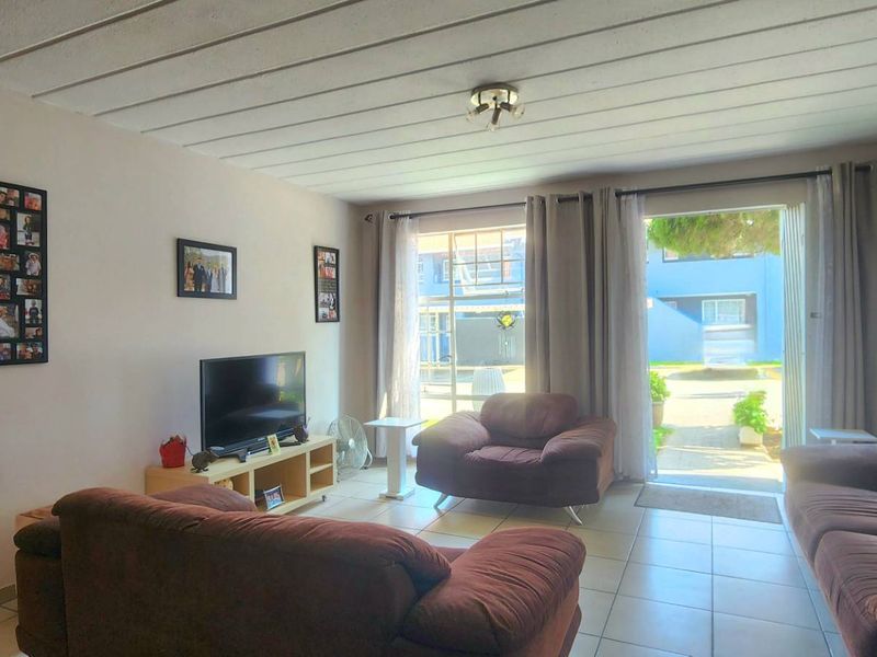 A comfortable living room featuring tiled flooring, an exposed beam ceiling, and a sliding glass door providing direct access to the outdoor area.