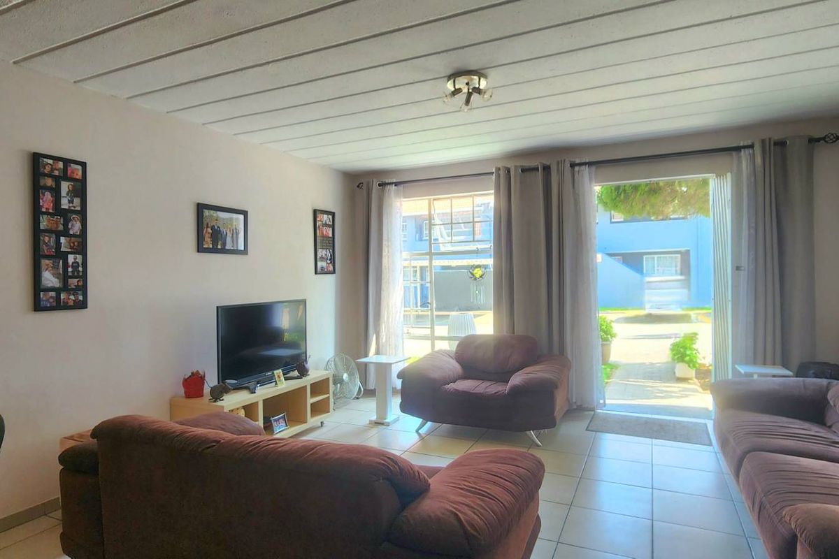 A comfortable living room featuring tiled flooring, an exposed beam ceiling, and a sliding glass door providing direct access to the outdoor area.