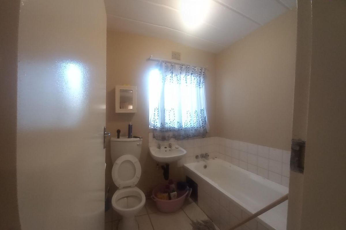 A functional bathroom featuring a standard bathtub, pedestal basin, and toilet, with neutral wall finishes and tiled flooring.
