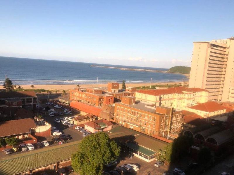 Elevated coastal view overlooking the beach, surrounding urban infrastructure, and nearby apartment buildings.