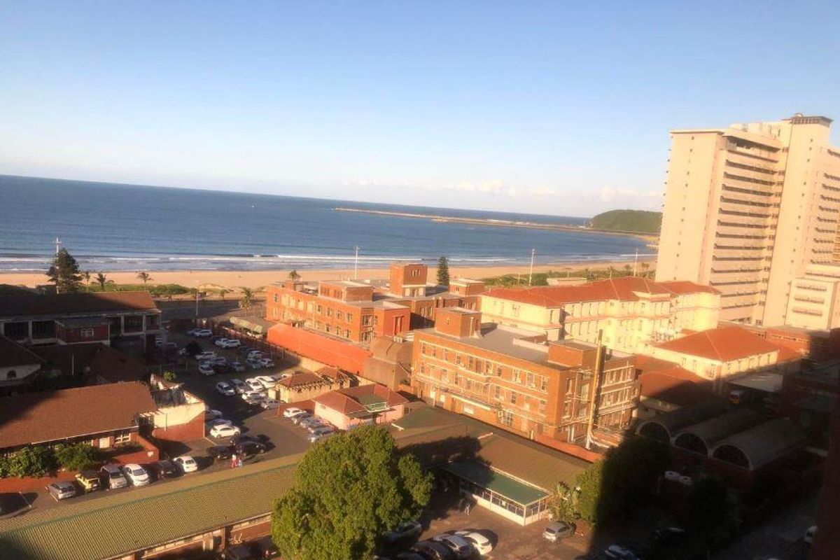 Elevated coastal view overlooking the beach, surrounding urban infrastructure, and nearby apartment buildings.