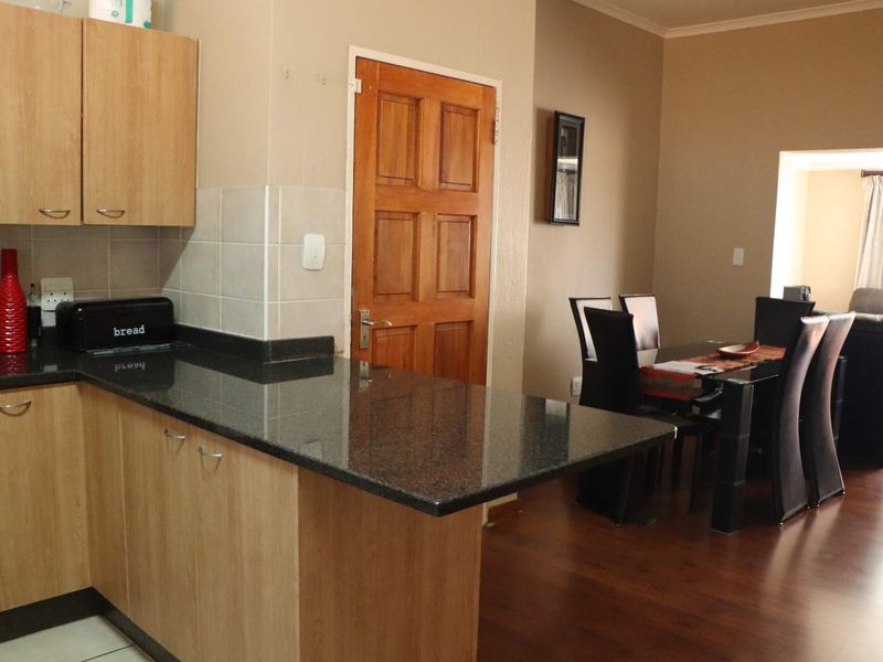 Open plan kitchen and dining area featuring granite countertops, light wood cabinetry, and laminate flooring, creating a functional and connected living space.
