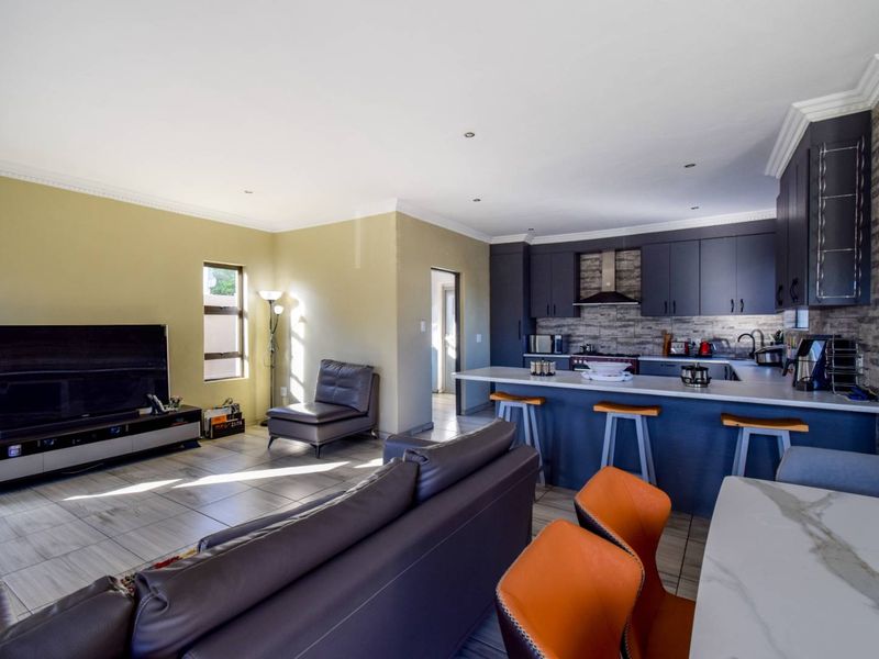 Open-plan living and kitchen area featuring dark cabinetry, a central island with breakfast bar seating, and neutral tiled flooring throughout.