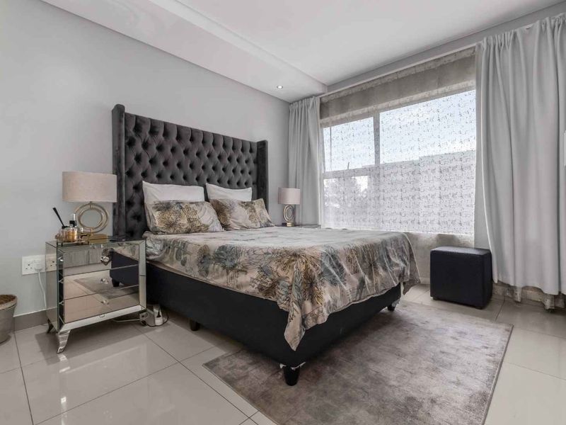 A well-maintained bedroom featuring tiled flooring, built-in cupboards, and a large window allowing for natural light.