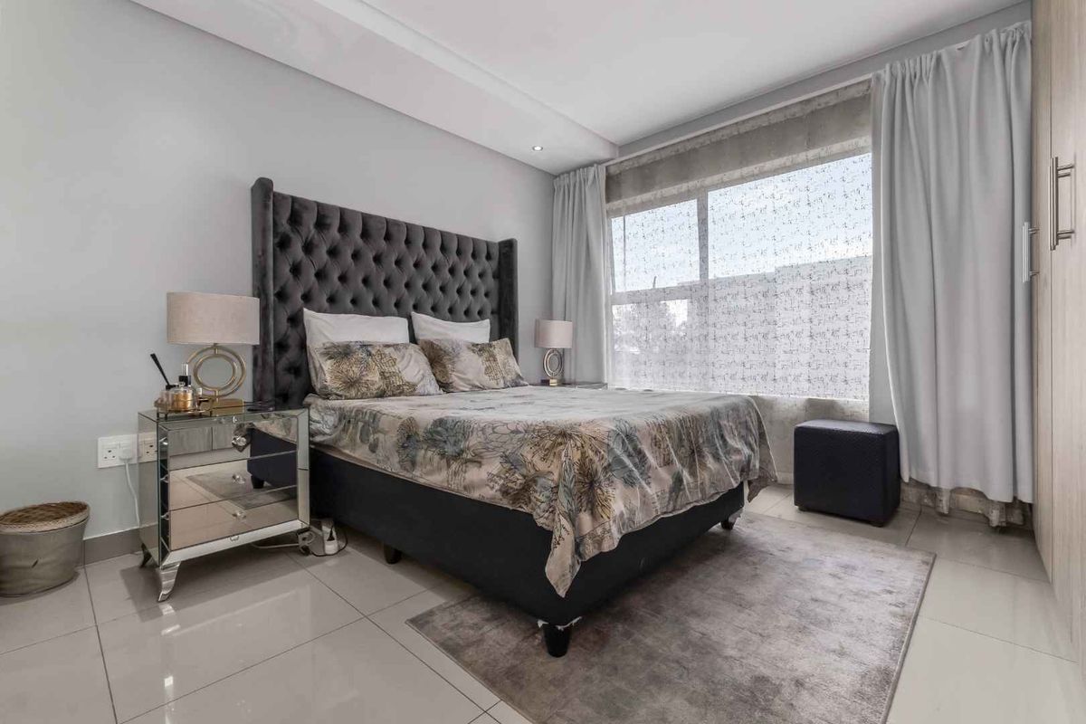 A well-maintained bedroom featuring tiled flooring, built-in cupboards, and a large window allowing for natural light.