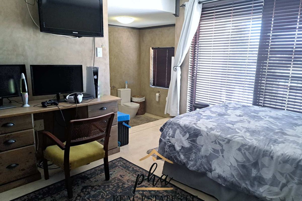 A bedroom featuring an open-plan layout with an integrated en-suite bathroom, tiled flooring, and large windows with venetian blinds.