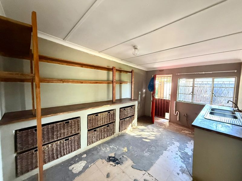 A functional scullery area featuring built-in shelving, a double sink, and direct exterior access via a security gate. The space requires floor refurbishment.