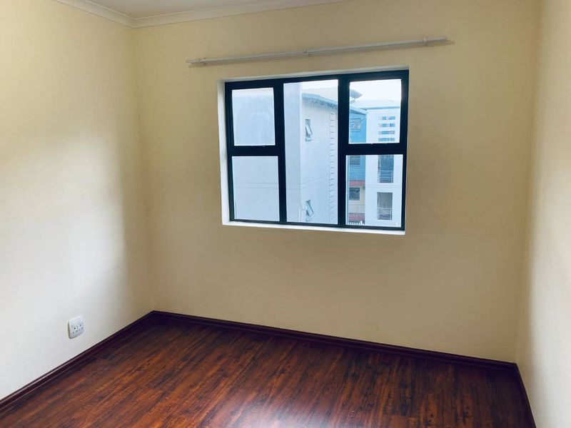 A clean, empty bedroom featuring dark laminate flooring, neutral walls, and an aluminium-framed window with a curtain rail.