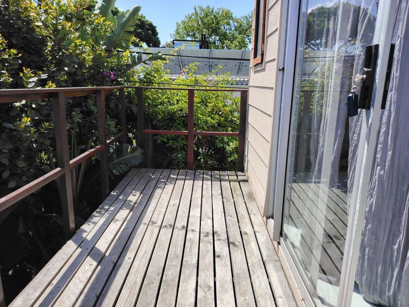 A compact timber balcony featuring a wooden balustrade and sliding glass door access, offering a private outdoor space.