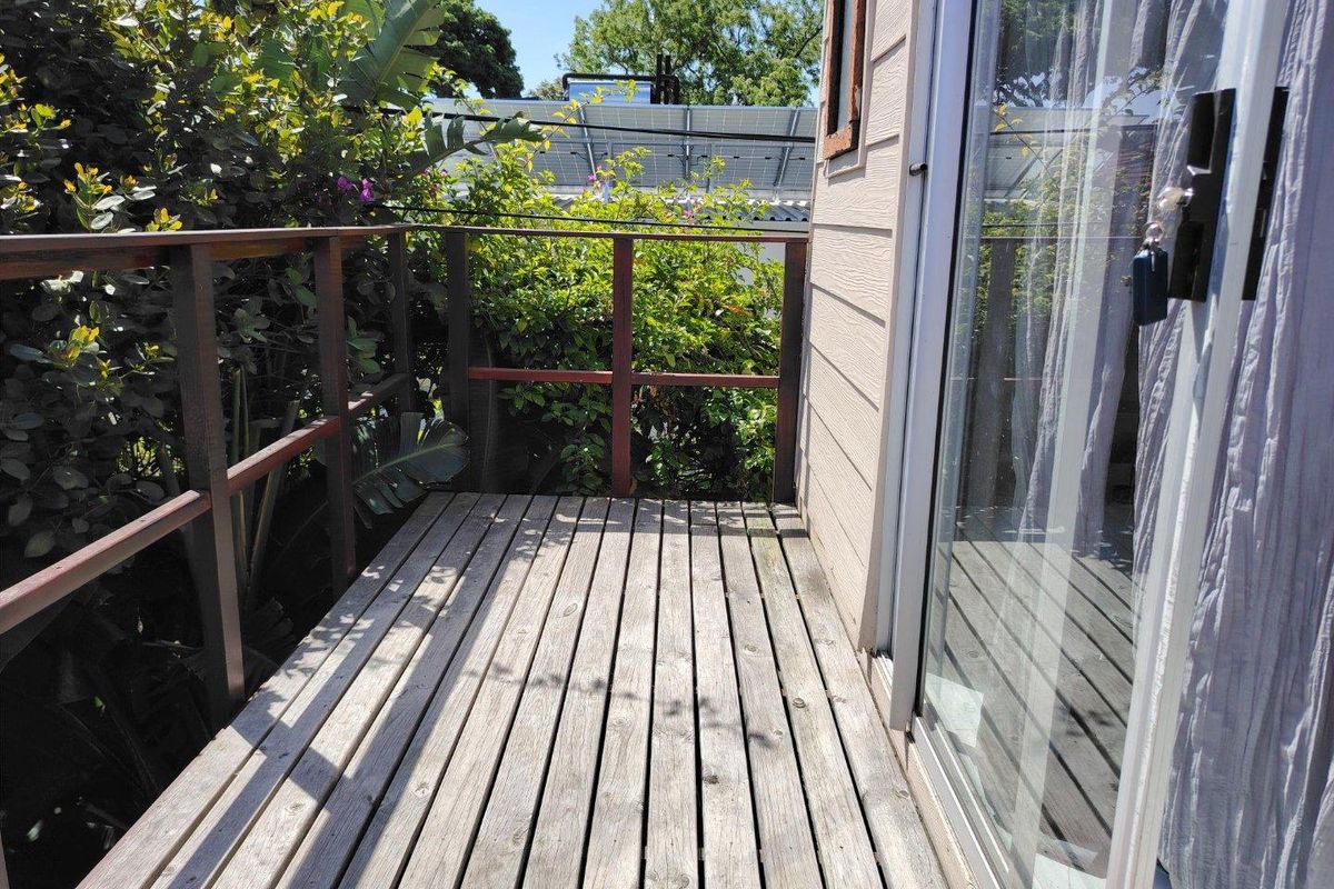 A compact timber balcony featuring a wooden balustrade and sliding glass door access, offering a private outdoor space.