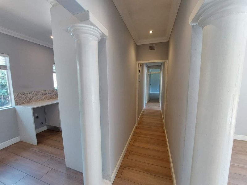 A bright, neutral hallway featuring decorative columns, modern laminate flooring, and recessed downlighting, leading through to the rest of the home.