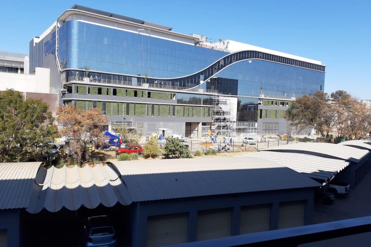 Exterior view of a modern commercial building featuring a glass facade and vertical garden, with a covered parking area in the foreground.
