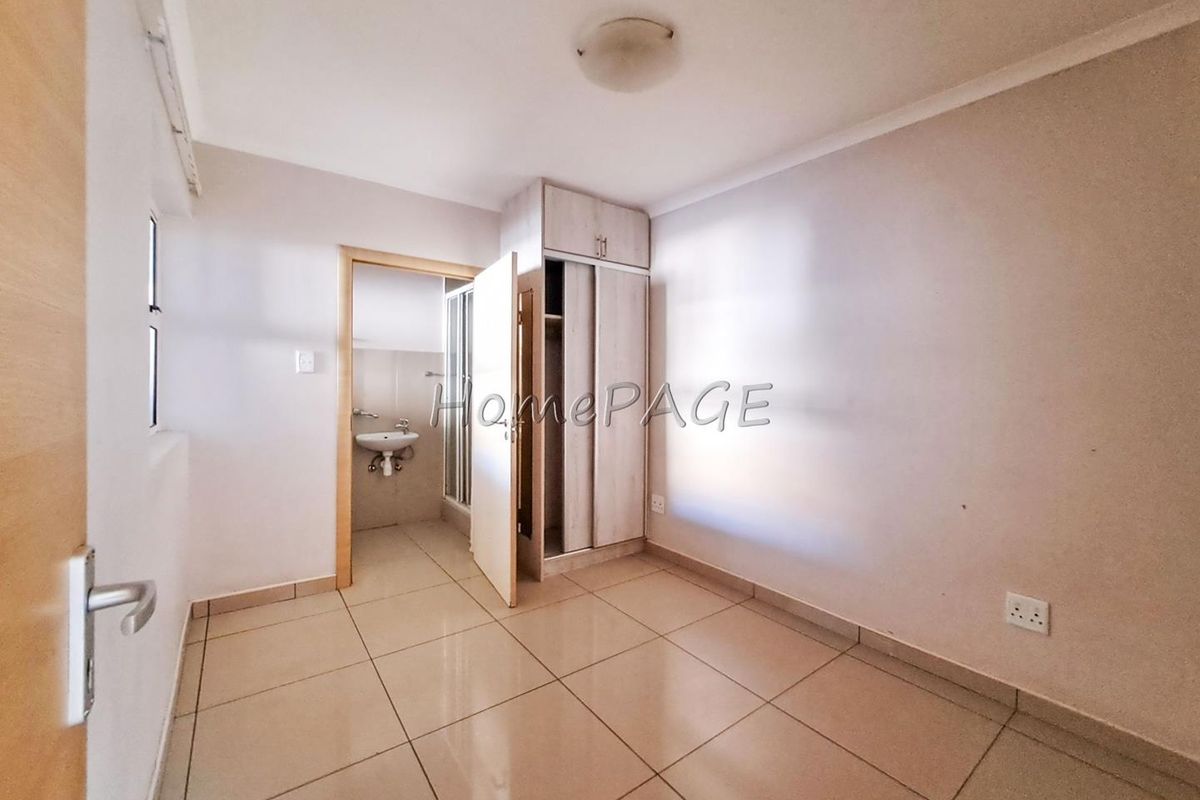A bedroom featuring tiled flooring and a built-in wardrobe, with an adjoining en-suite bathroom visible through the doorway.