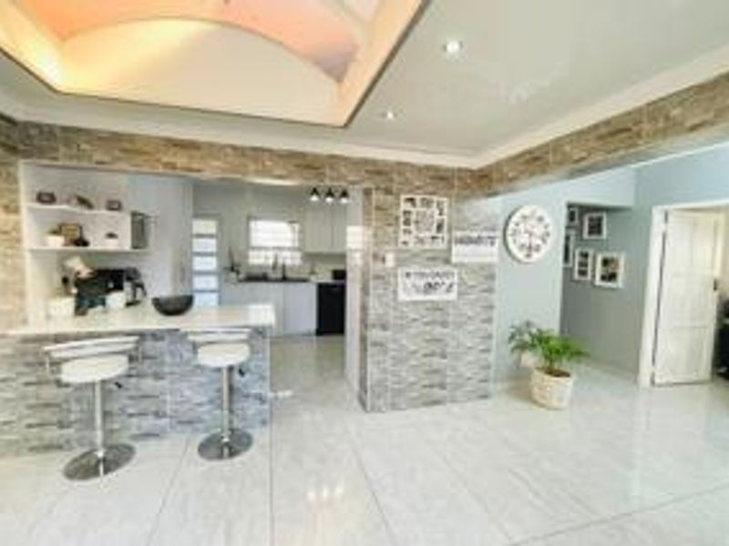 Open plan living area featuring a breakfast bar with stone veneer cladding, recessed ceiling details, and polished tiled flooring throughout.