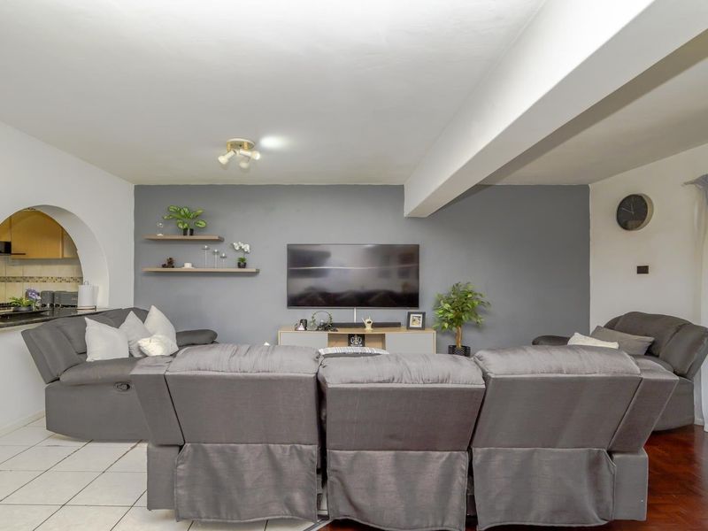Open plan living area featuring a distinct archway leading to the kitchen, with a mix of tiled and hardwood flooring and a feature wall.