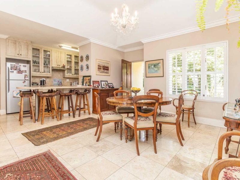 Open-plan kitchen and dining area featuring tiled flooring, built-in cabinetry, a breakfast bar, and plantation shutters, offering a functional and well-lit living space.