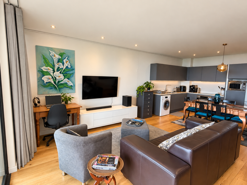 A modern open-plan living area featuring hardwood floors, recessed lighting, and a sleek, fully equipped kitchen with integrated appliances.