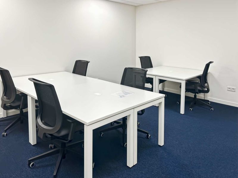 A clean, functional office space featuring blue carpeting, white walls, and a suspended ceiling, suitable for a professional work environment.