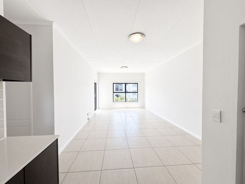 A bright and spacious open-plan living area featuring neutral tiled flooring, clean white walls, and modern recessed lighting, offering a versatile blank canvas.