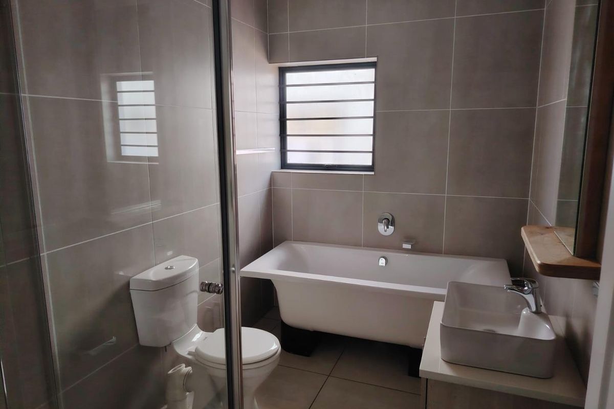 Modern bathroom featuring a freestanding bathtub, glass-enclosed shower, wall-mounted basin, and neutral floor-to-ceiling tiling.